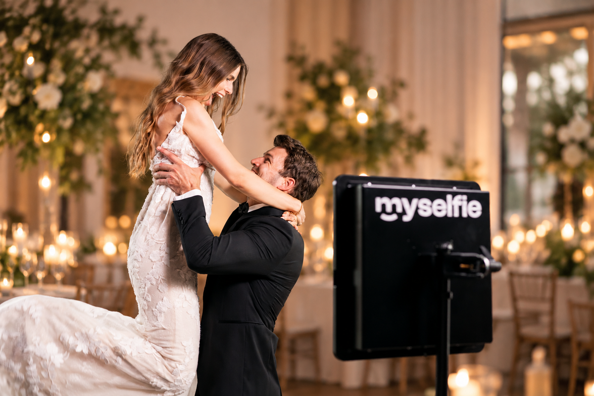 Gommen løfter bruden op ved siden af Myselfie photo booth i den pyntede festsal