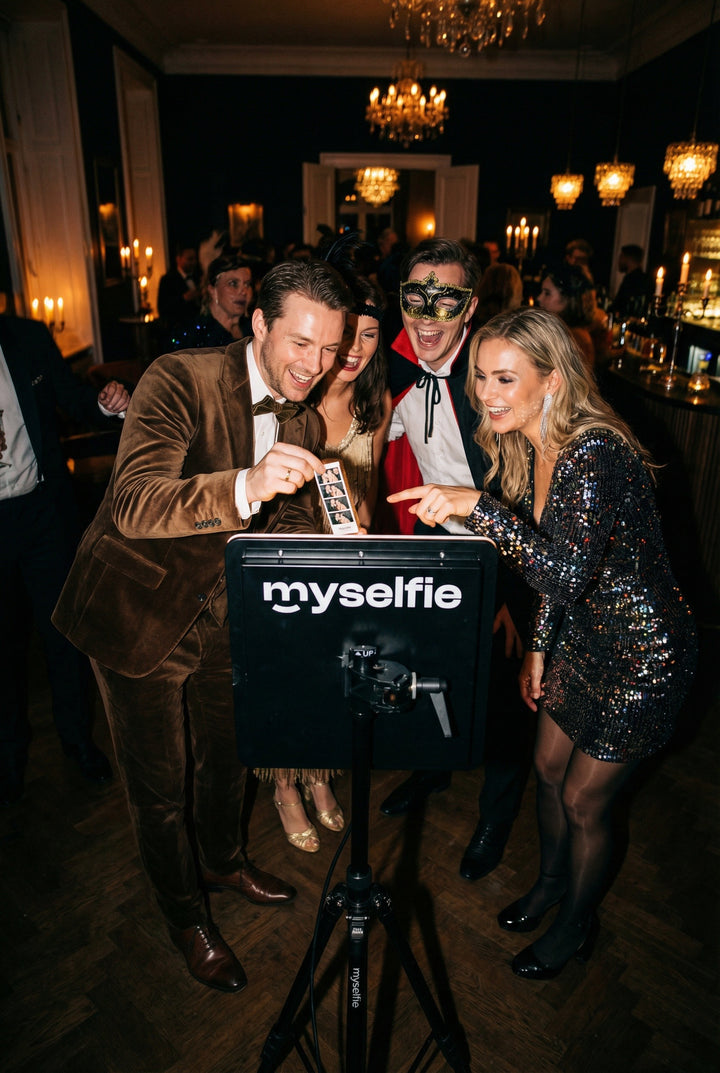 Gæster i festtøj og maske griner og tager billeder ved Myselfie photo booth til en temafest