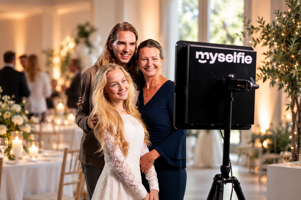 Konfirmand og forældre smiler foran Myselfie photo booth i festlokalet